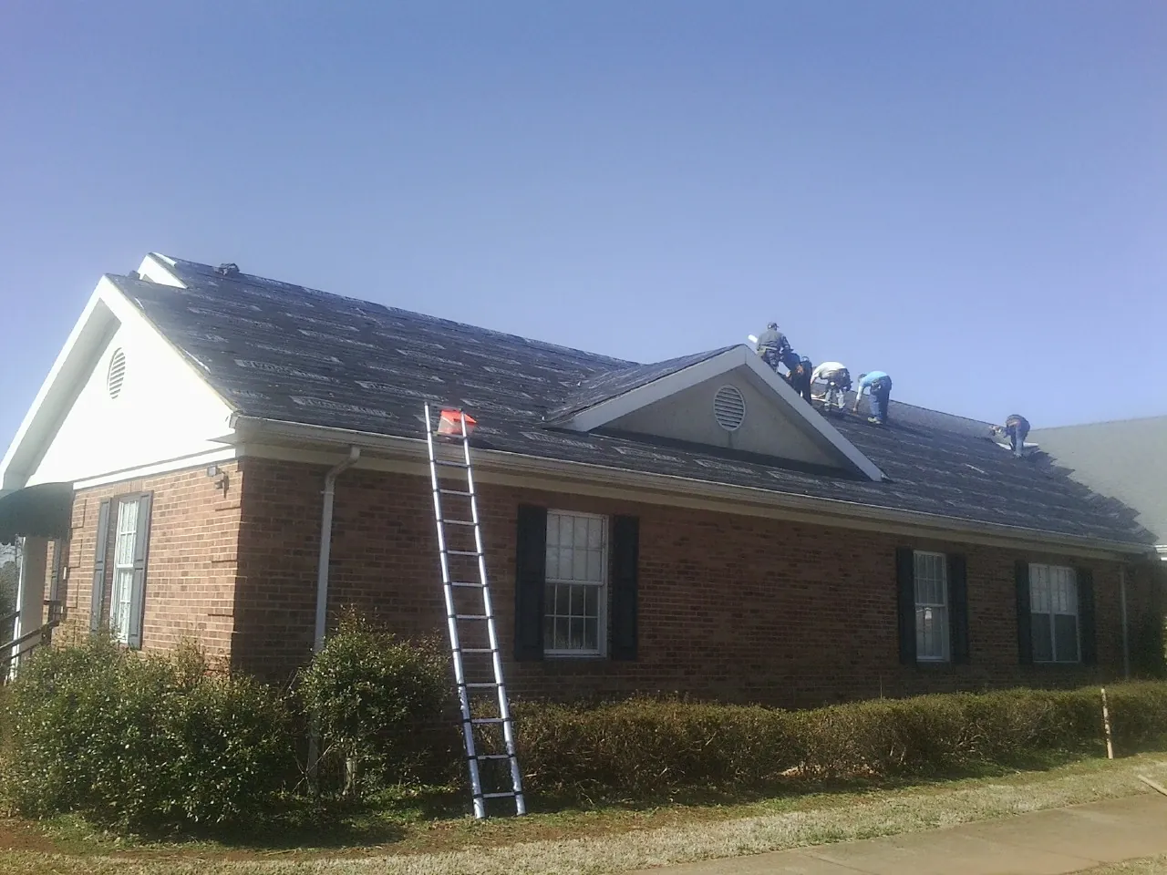 Crew tearing shingles off a brick ranch roof with a ladder set — Emergency Roof Repair work by our crew in Olympia Fields