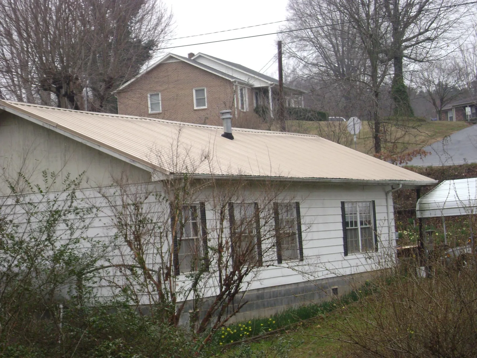 Tan metal roof on a white sided house set into a hillside — Commercial Roofing by Roofing Brothers in Olympia Fields